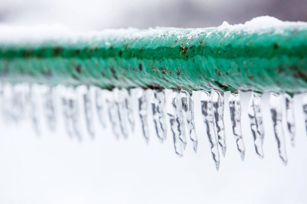 Icicles dripping down a narrow green pipe.