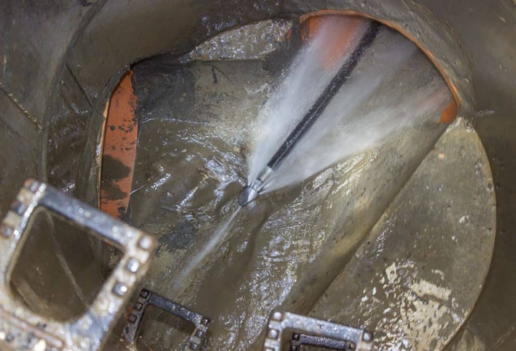 A high-pressure water jet cleans the interior of a large underground drain pipe, flushing away accumulated dirt and buildup.
